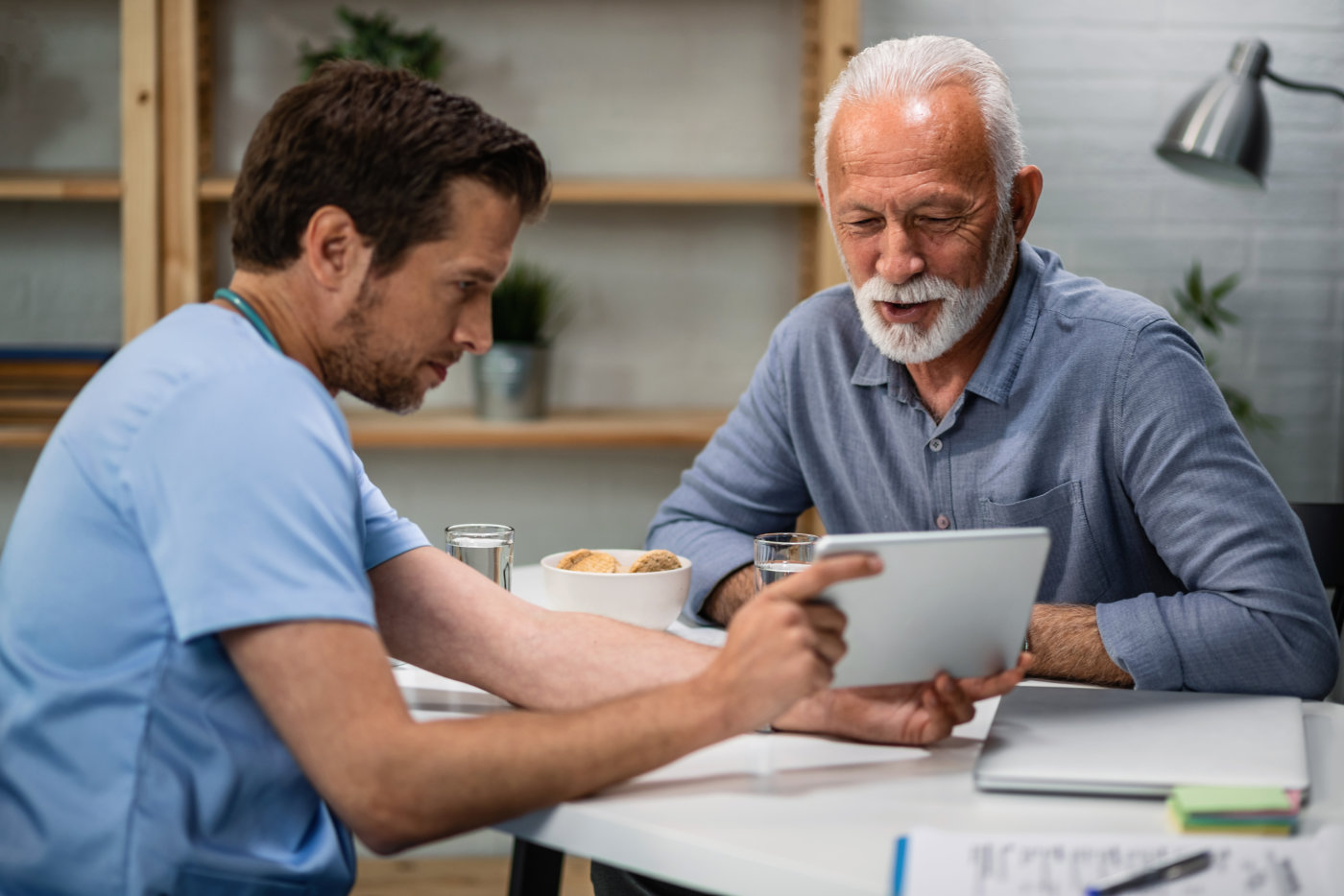 Happy senior patient and his doctor looking at medical test results on touchpad during medical appointment.