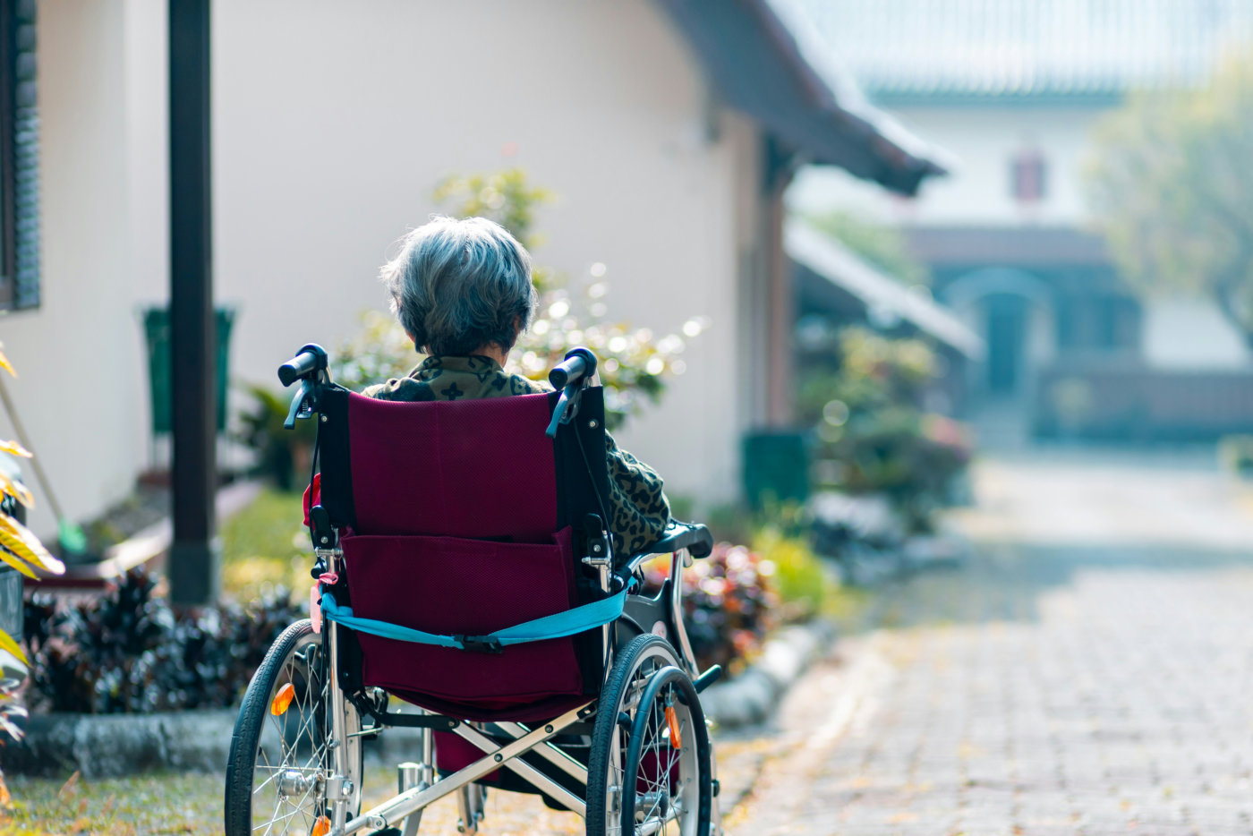 A senior woman in a wheelchair is being guided down a street, experiencing the sights and sounds of her neighborhood.