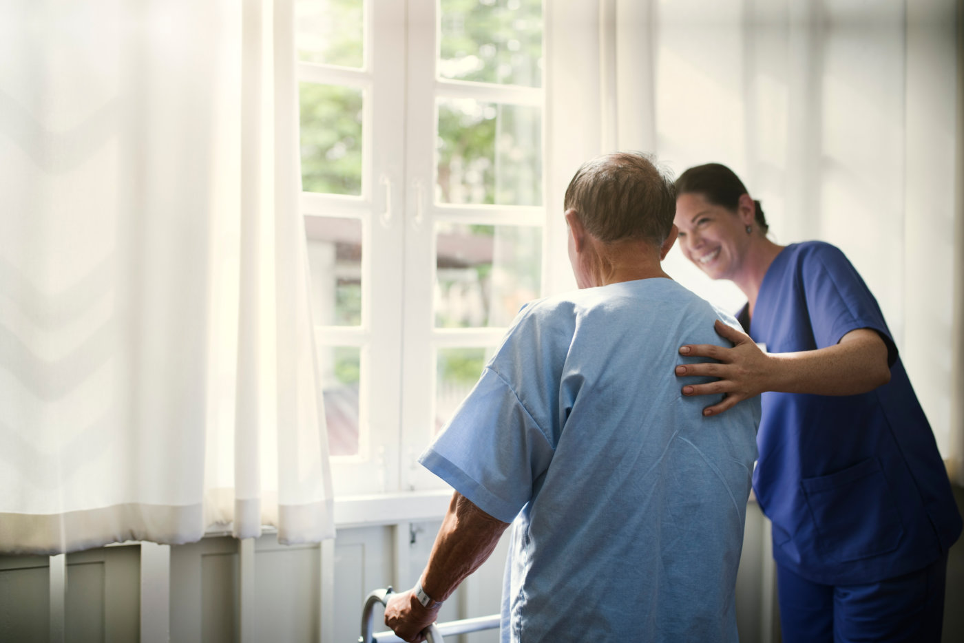 A nurse supports an elderly man with a walker, demonstrating kindness and assistance in a healthcare setting.