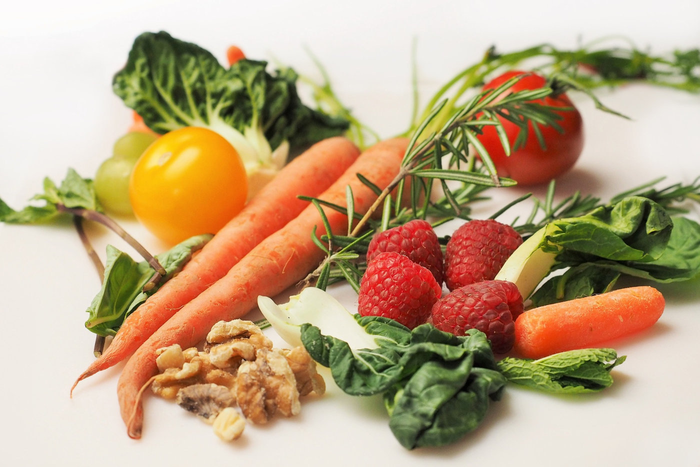 A diverse selection of fresh produce, showcasing carrots, raspberries, walnuts, and spinach in a visually appealing display.