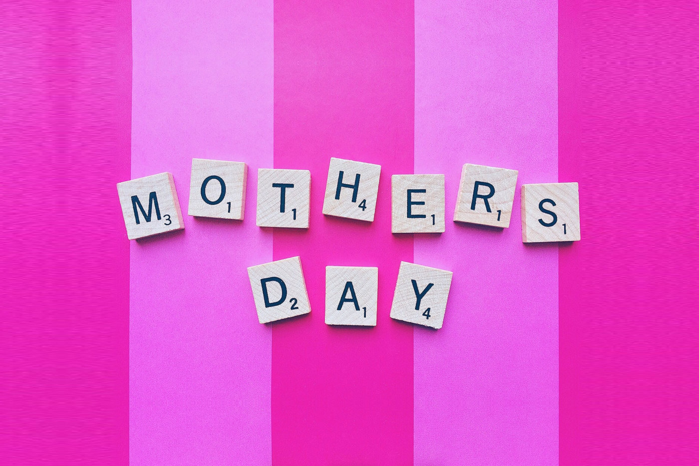 Scrabble letters spell "Mother's Day" on a pink striped background